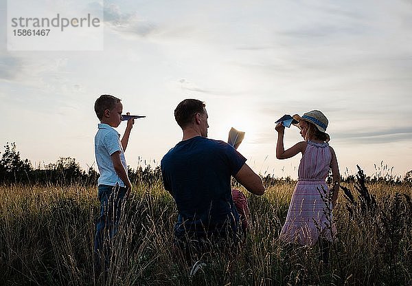 Vater spielt mit seinem Sohn & seiner Tochter bei Sonnenuntergang Papierflieger