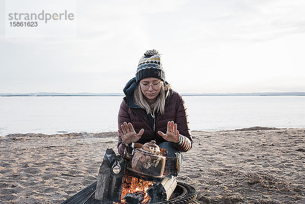 Frau  die ihre Hände am Lagerfeuer wärmt und darauf wartet  dass das Wasser kocht
