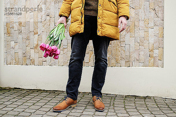 blonder Mann in einer gelben Winterjacke mit einem Tulpenstrauss in der Hand
