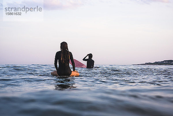 Wasserfreundinnen surfen gemeinsam bei Sonnenuntergang