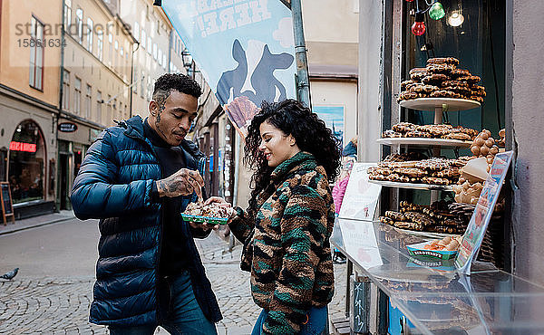 ein Paar  das auf der Straße gemeinsam lächelnd und lachend das Essen teilt