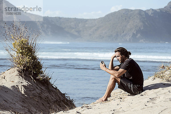 Mann benutzt Smartphone am Strand