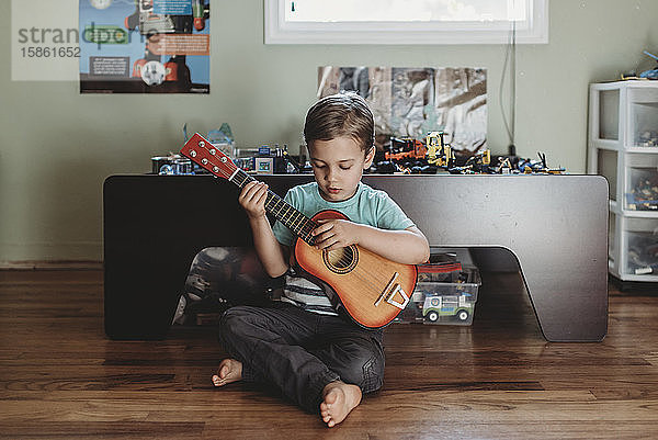 5 Jahre alter Junge sitzt auf Hartholzboden und spielt Gitarre