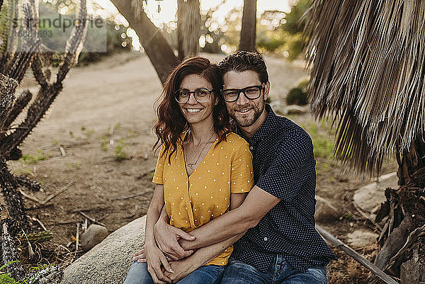 Mittelgroßes  erwachsenes Ehepaar sitzt auf einem Felsen und lächelt  während sie sich umarmen