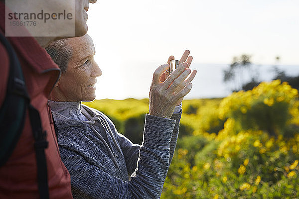 Mann steht neben älterer Frau  die mit einem Smartphone fotografiert  während sie sich gegen den Himmel stellt