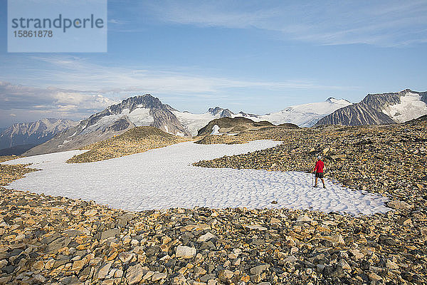 Wanderer überquert Schneefeld in felsigem Gelände.
