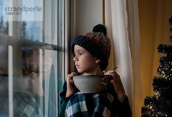 Junge saß auf einem Fensterbrett mit einer Müslischale und schaute nach draußen