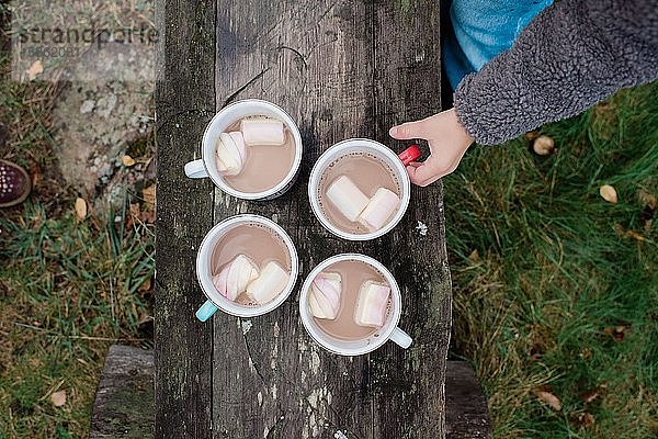 heiße Schokolade und Marshmallows auf einer Bank im Freien mit der Hand eines Jungen