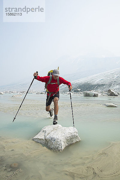 Backpacker springt über den Bach auf einen Felsblock in Gletschernähe.