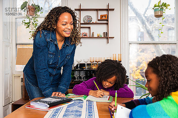 Lächelnde Mutter hilft Töchtern zu Hause beim Studium