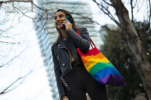 Schöne lesbische Frau mit einer Pride-Tasche  die am Telefon spricht.