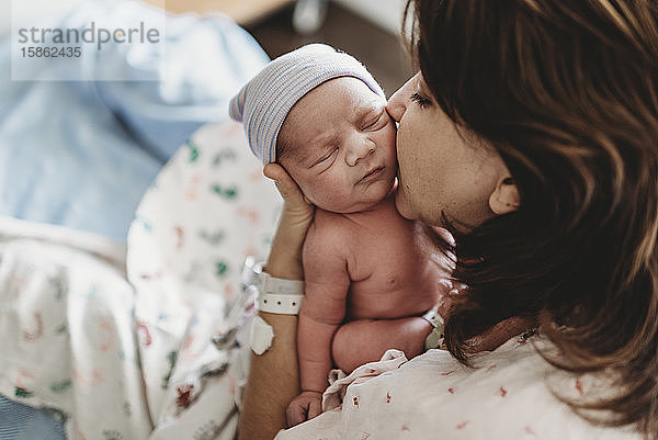 Detailaufnahme einer Mutter  die im Krankenhaus ein Neugeborenes auf die Wange küsst