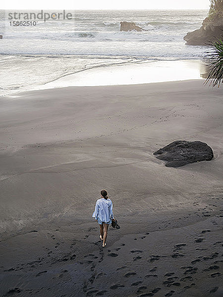 Junge Frau  die an einem felsigen Strand spazieren geht und die Aussicht betrachtet