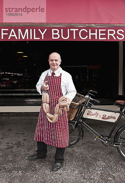 Metzger hält Wurst vor seinem Laden