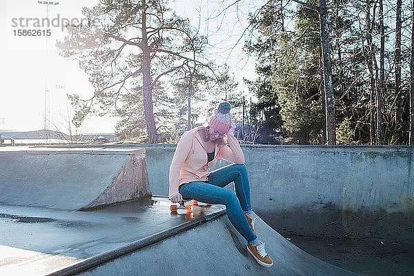 Frau saß auf einem Brett in einem Skatepark bei Sonnenschein