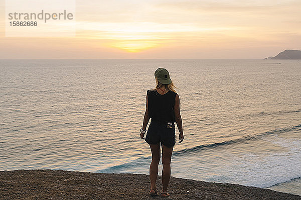 Junge Frau steht bei Sonnenuntergang auf einem Felsen am Strand