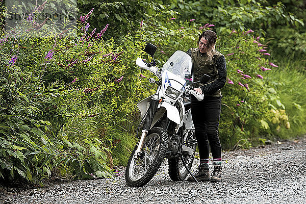 Eine Frau macht eine Pause vom Motorradfahren und steht mit ihrem Motorrad.