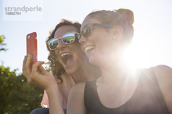 Zwei Freundinnen lächeln für ein Selfie im Sonnenschein.