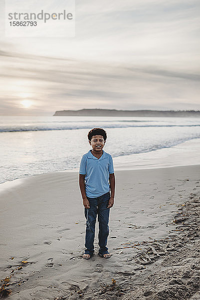 Porträt eines jungen Jungen im Schulalter  der bei Sonnenuntergang am Strand lächelt