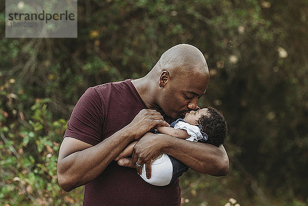 Nahaufnahme glücklicher Vater hält und küsst neugeborenes Mädchen draußen