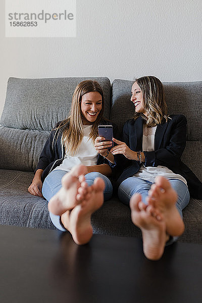 Zwei glückliche Mädchen auf einer Couch mit Füßen auf einem Tisch