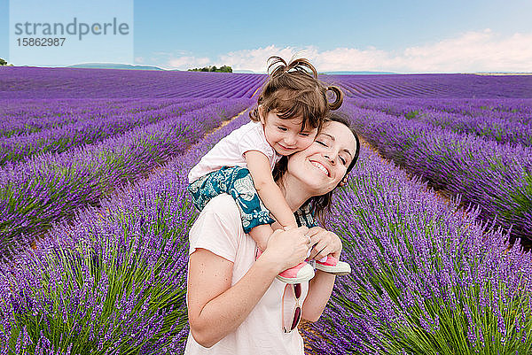 Glückliche Frau und kleines Mädchen spazieren im Sommer zwischen Lavendelfeldern