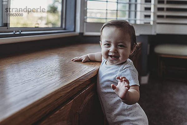 Glücklich lächelndes Baby mit zwei Zähnen am Fenster stehend