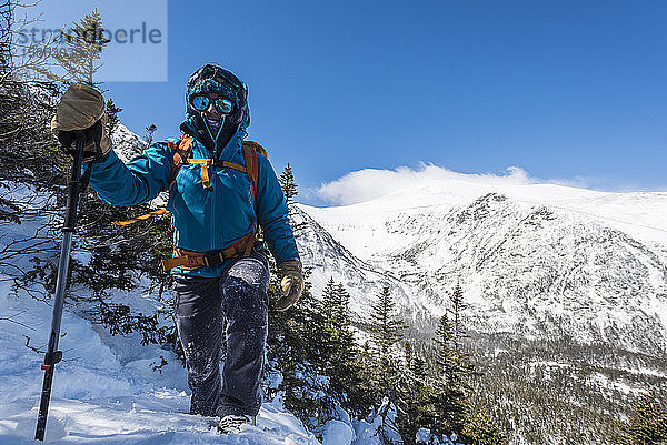 Eine Frau  die allein einen verschneiten Hang hinunterwandert  mit der Tuckerman-Schlucht und dem Gipfel des Mount Washington im Hintergrund.