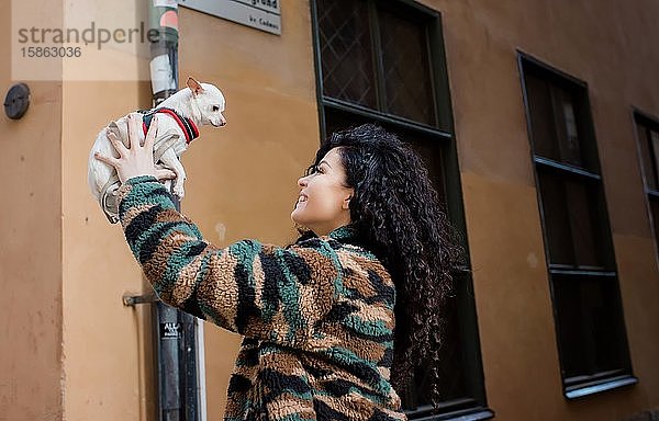 Frau  die ihren Hund lächelnd in die Luft hält