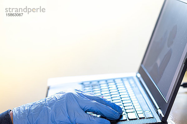 Ein Mann mit blauen Handschuhen arbeitet von zu Hause aus an seinem Laptop  Coronavirus