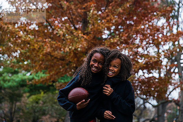 Fröhliche Schwestern mit American Football im Herbst im Park