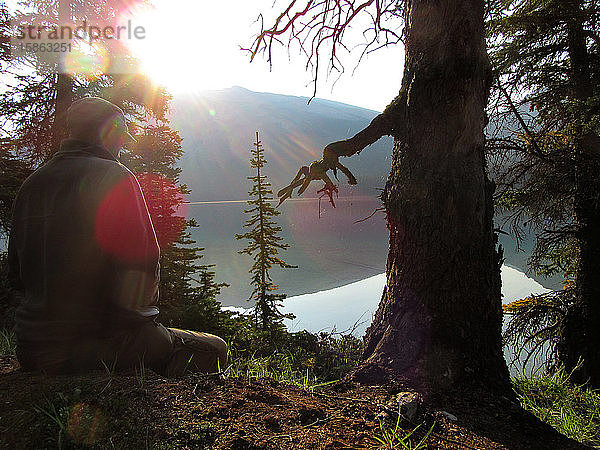 Junger Mann meditiert allein am stillen Bergsee bei Sonnenaufgang