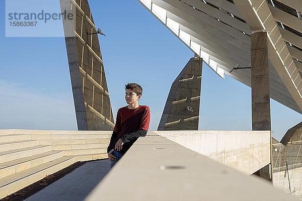 Junger fröhlicher Teenager  der an einer Wand lehnt und an einem sonnigen Tag wegschaut