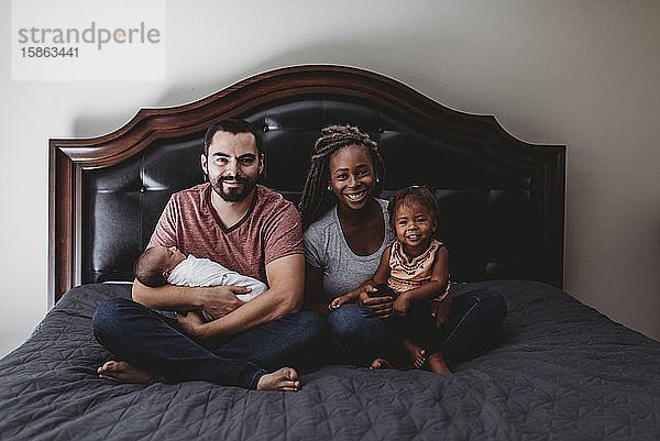 Glückliche multirassische Familie im Bett mit Vater und Kleinkind und Mutter und 2 Jahre alt