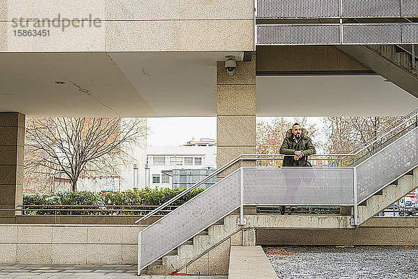 Bärtiger Hipster-Mann entspannt sich auf einer Treppe in einem Gebäudekomplex