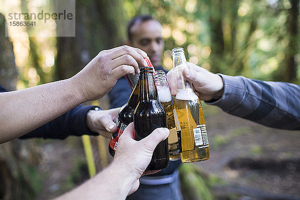 Männer jubeln im Wald ihren Bierflaschen zu.