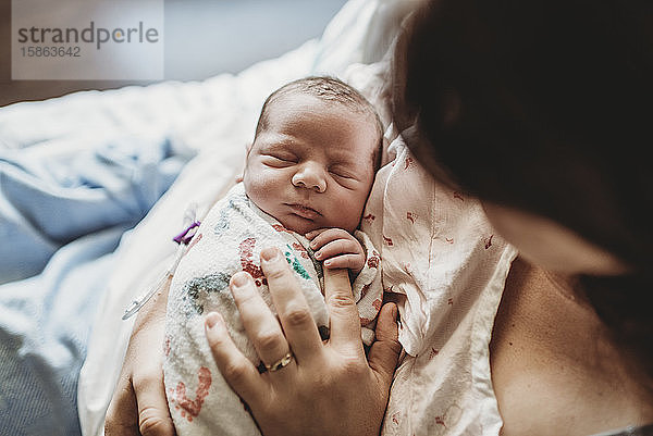 Draufsicht der Mutter  die die Finger des neugeborenen Jungen im Krankenhausbett hält