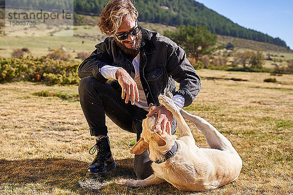 Porträt eines jungen tätowierten Mannes  der mit seinem Hund auf dem Land spielt