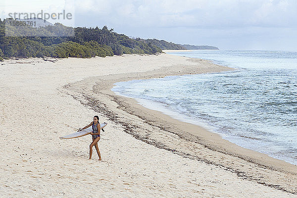 Junge Frau mit Surfbrett am Strand spazieren gehen