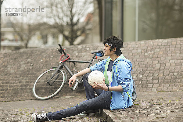 junger Mann mit Ball im Freien sitzend