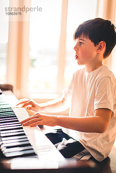 Der Junge konzentrierte sich beim Klavierspielen in einem sonnigen Raum.