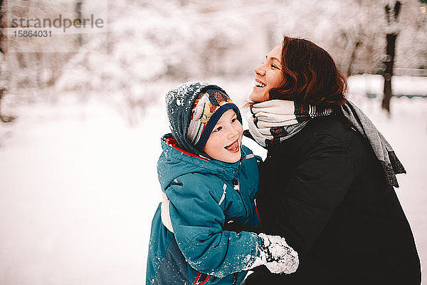 Glückliche Mutter umarmt verspielten Sohn im Winter im Park