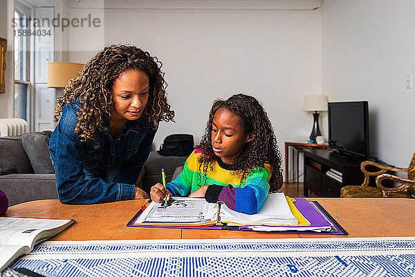 Mutter hilft der Tochter bei den Hausaufgaben bei Tisch im Wohnzimmer