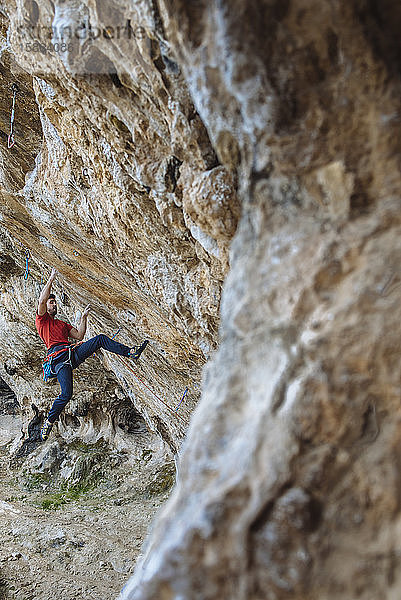 Bergsteiger  der eine harte Sportkletterroute in einer Höhle beginnt.