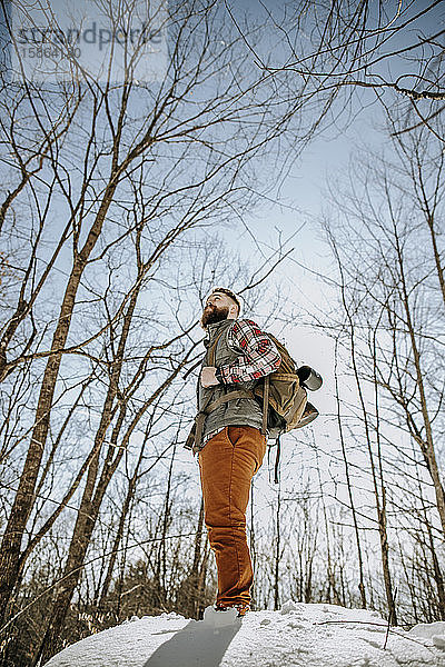 Mann mit Bart schaut beim Wandern in verschneiten Wäldern in die Ferne