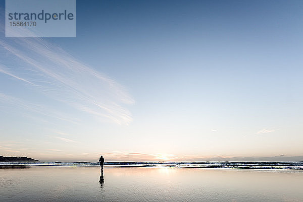 Silhouette einer Person  die bei Sonnenaufgang am friedlichen Strand spazieren geht