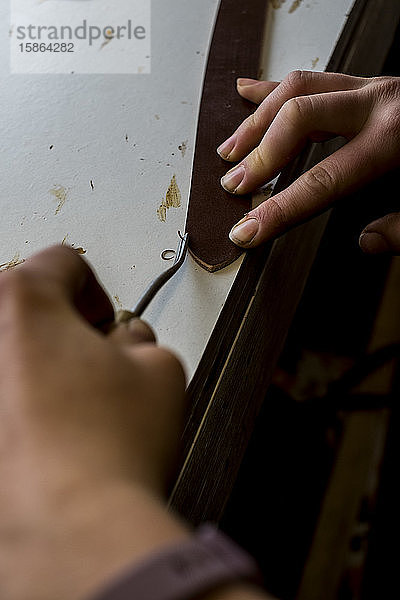 Nahaufnahme einer Person  die in einer Sattlerwerkstatt arbeitet  mit einem Handwerkzeug an einem Lederriemen.