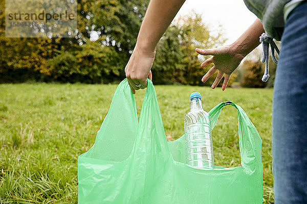 Frau stopft Weichplastikabfälle in eine große Plastikflasche  um einen Ökoblock als Baustein herzustellen