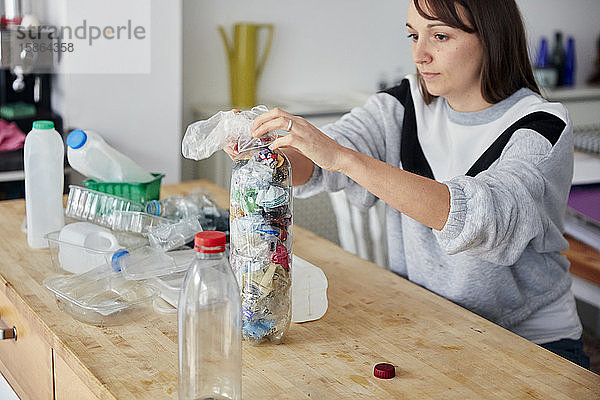 Frau stopft Weichplastikabfälle in eine große Plastikflasche  um einen Ökoblock als Baustein herzustellen