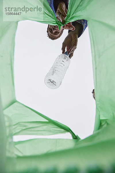 Mann lässt eine Plastikflasche in eine grüne Plastiktüte fallen  Blick aus der Innentasche.